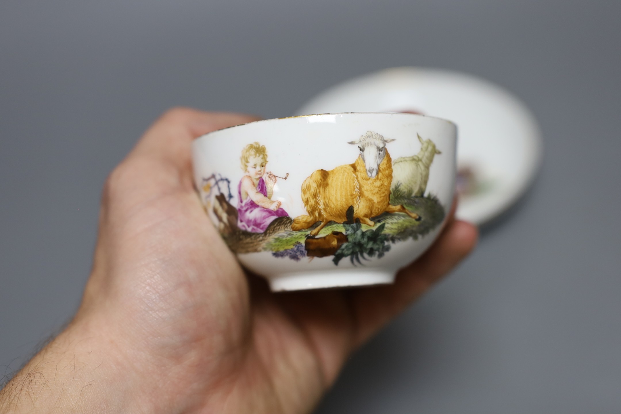 A Meissen teacup and saucer painted with a landscape with children in robes with recumbent sheep, crossed swords mark and dot in underglaze-blue, impressed numerals, saucer 13.5 cms diameter